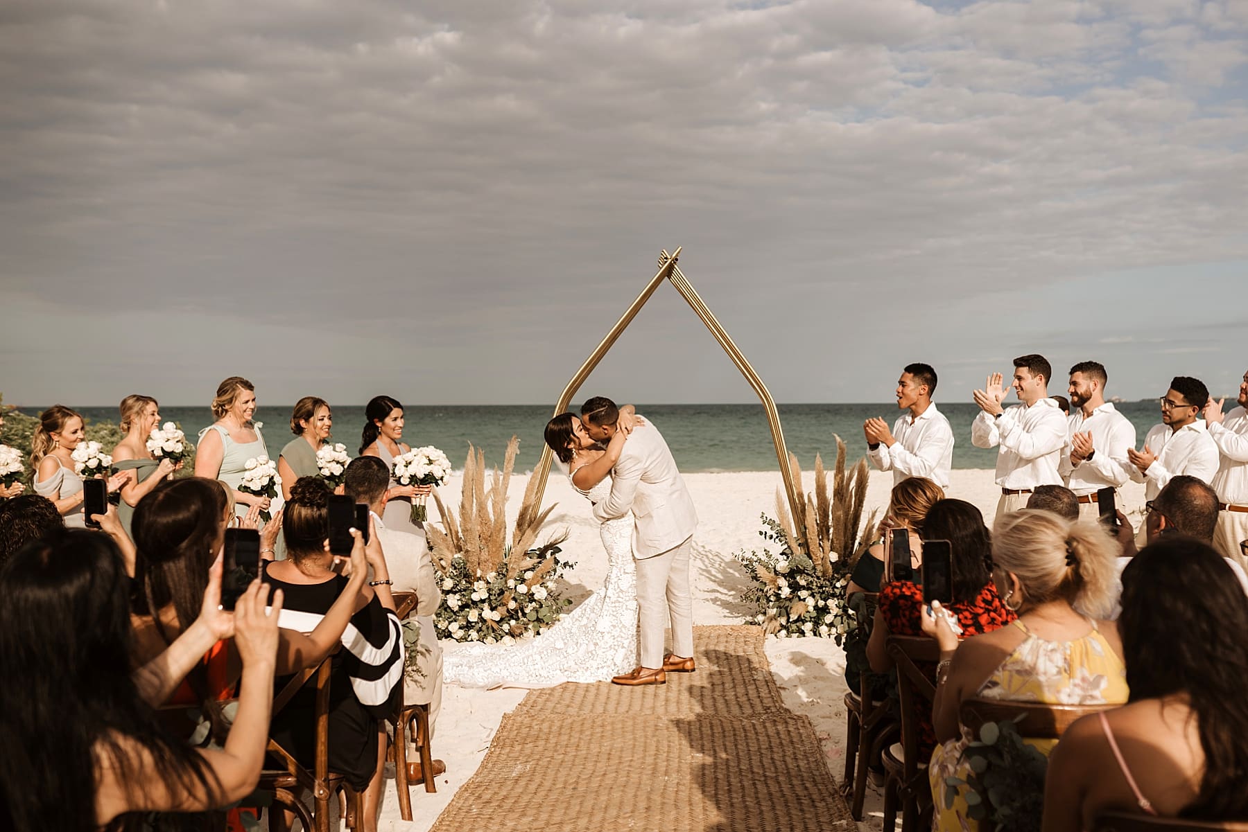 First kiss as husband and wife during beach wedding ceremony under metal arch