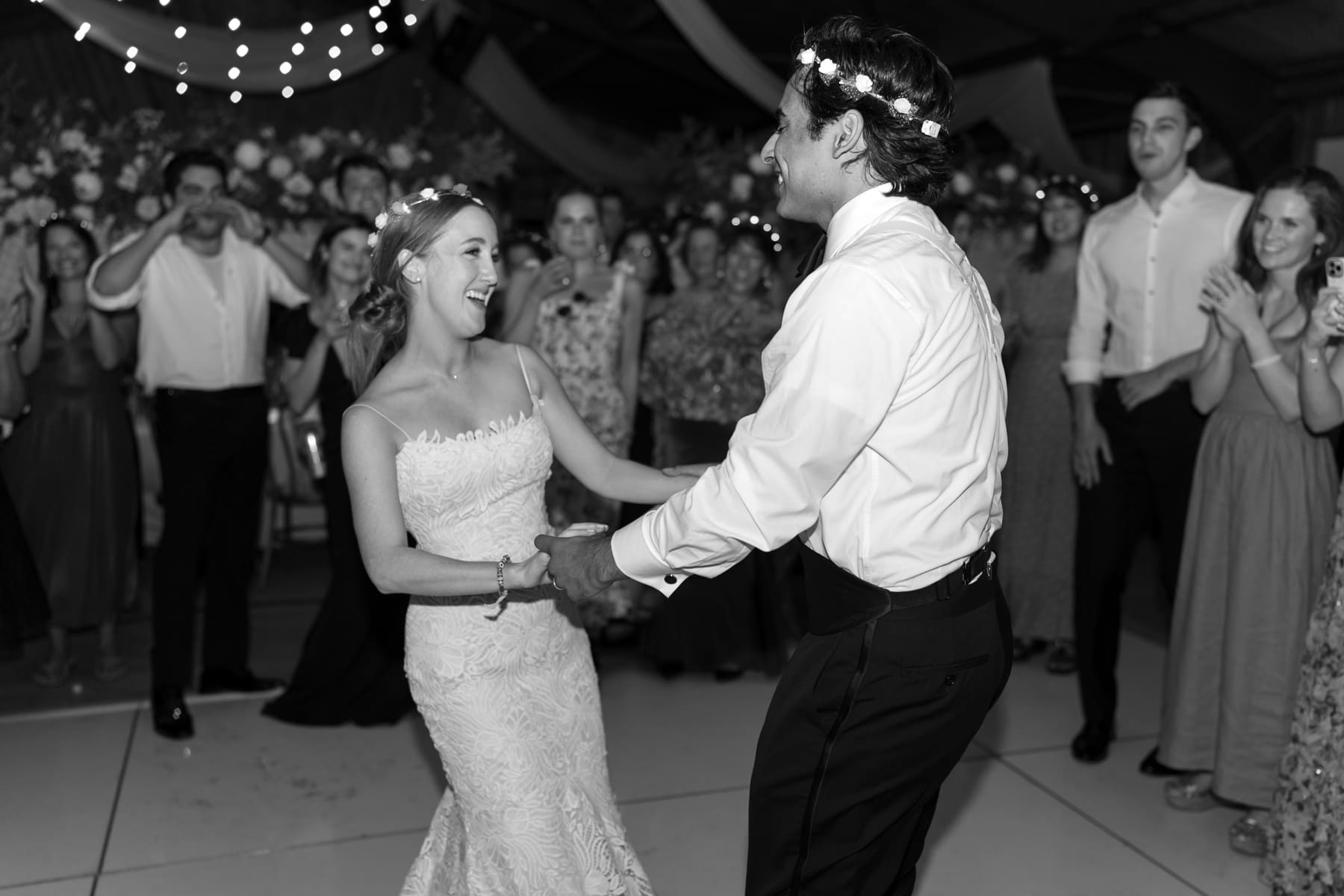 Bride and groom dancing while wearing floral crowns at reception 