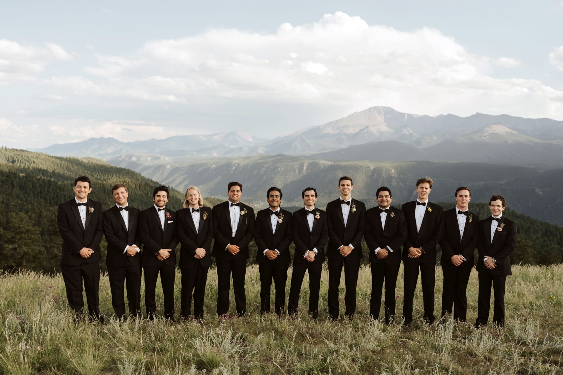 Groom with groomsmen in black tuxes standing in front of mountains at destination Colorado wedding