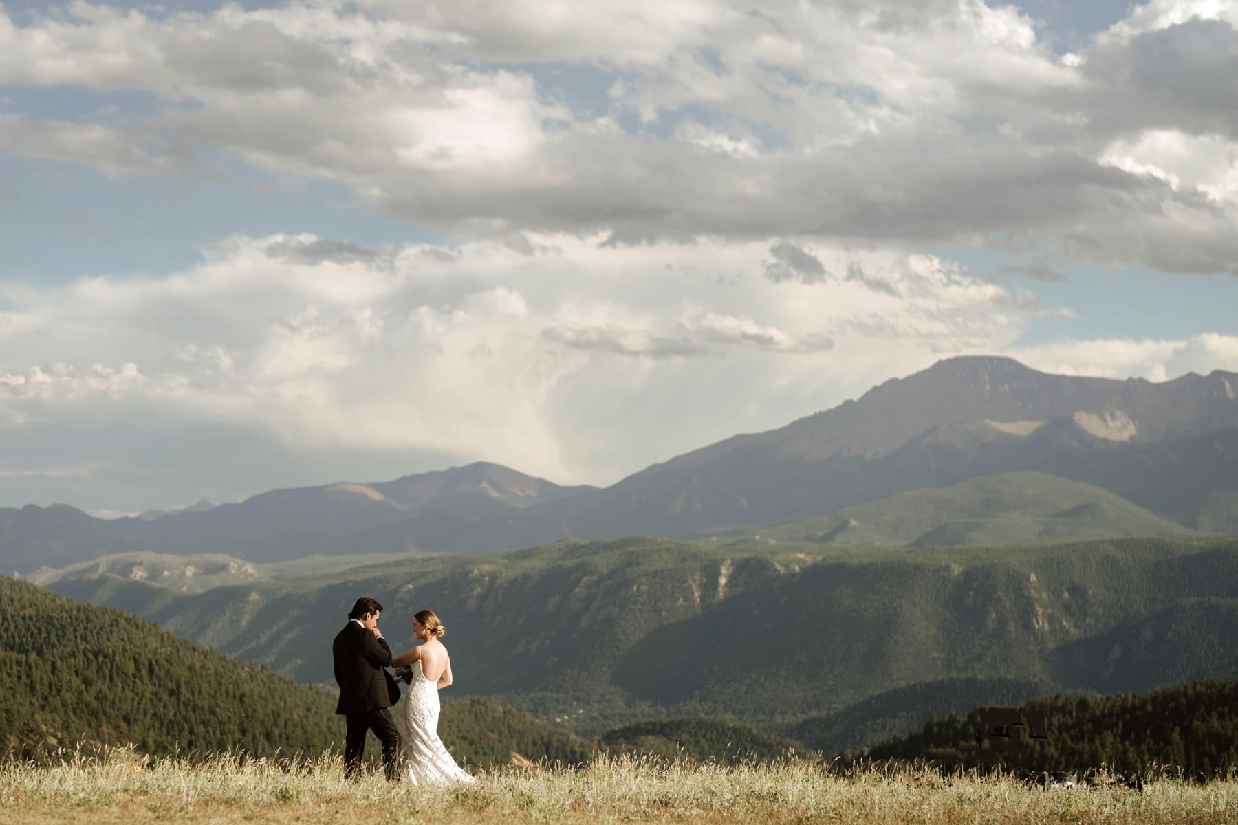 Groom kissing brides hand as they stand in front of the Rocky Mountains after destination Colorado wedding  
