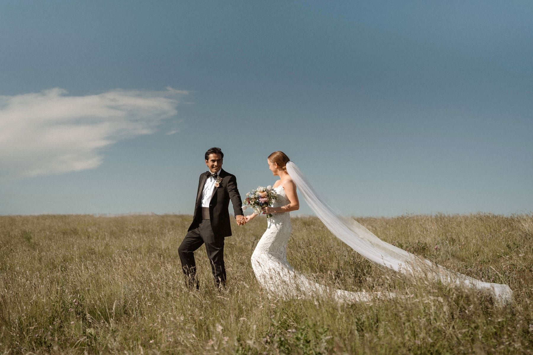 Bride and groom holding hands while walking in field in Colorado 
