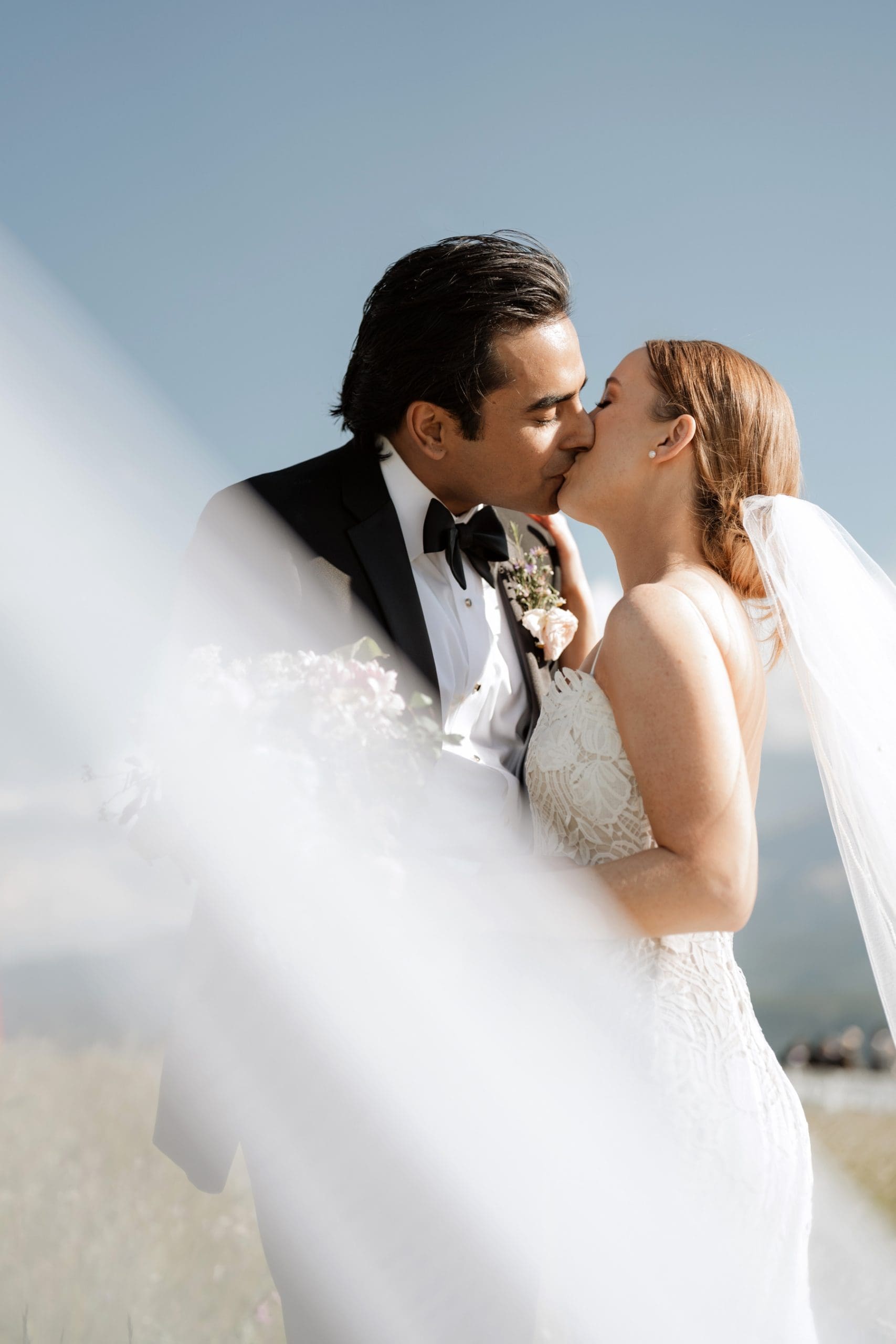 Bride and groom kissing with brides veil flowing in front of them