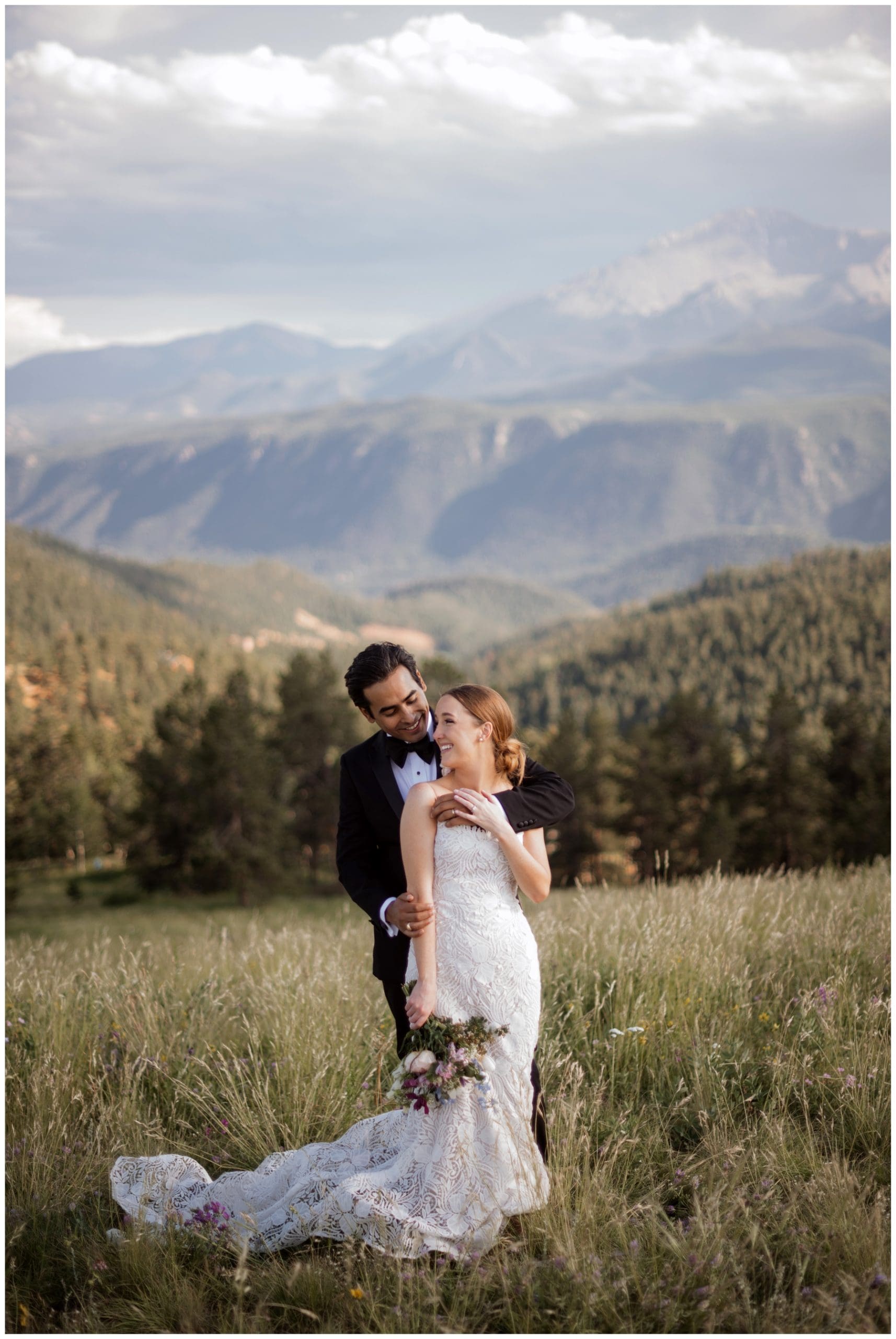 Bride looking up at groom standing behind her in field in front of mountains