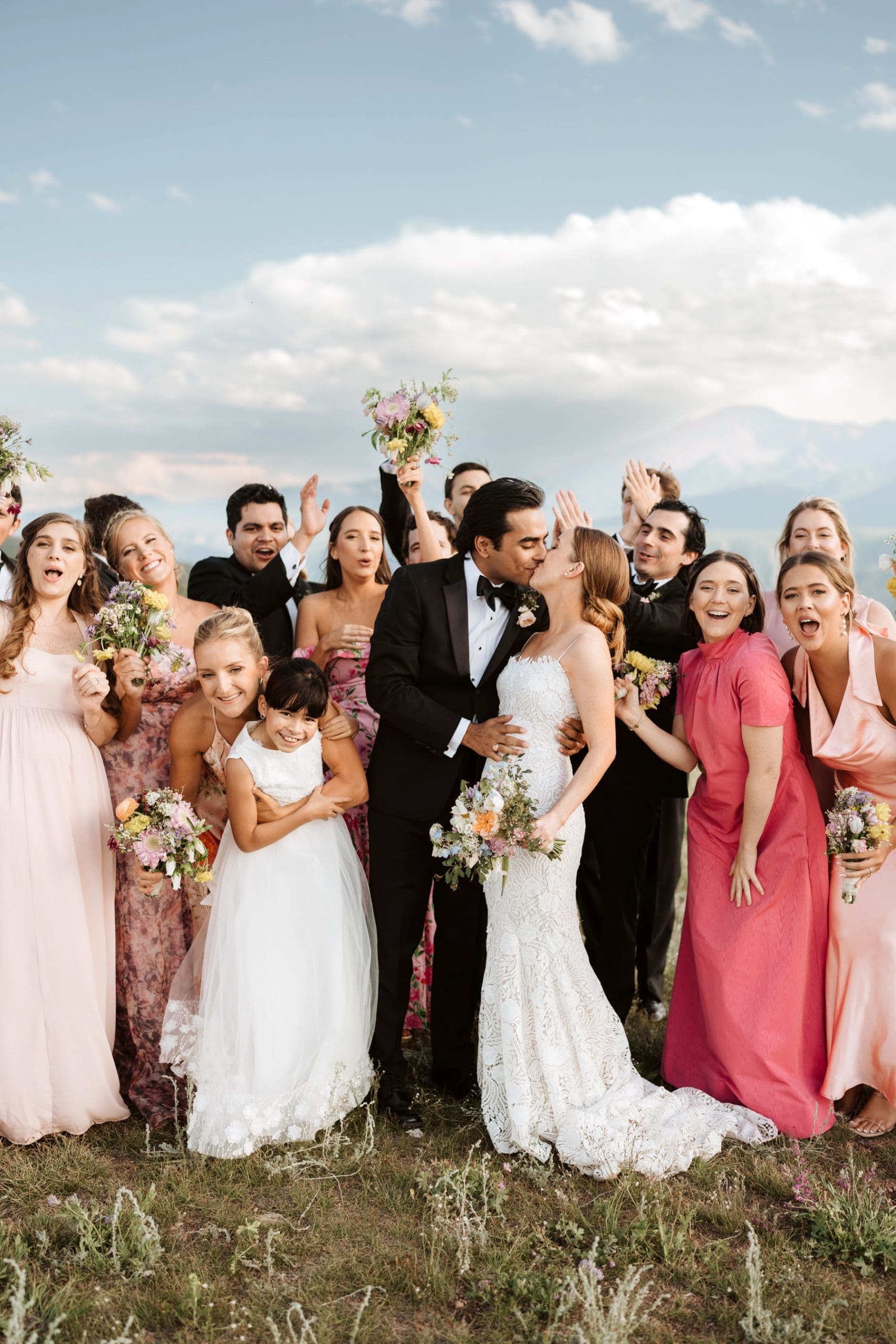 Bridal party cheering behind couple as they kiss