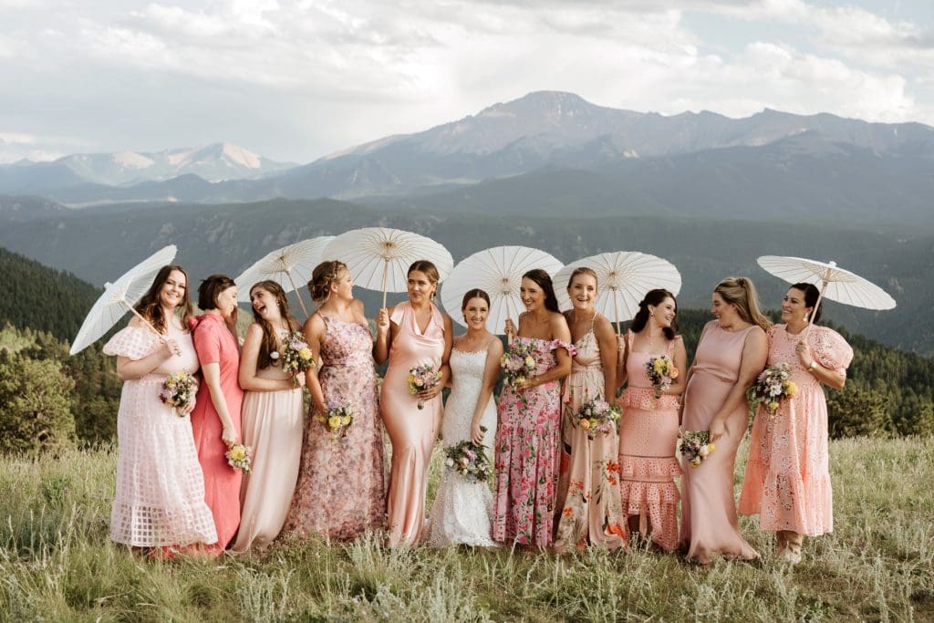 Bride and bridesmaids holding parasols in front of the Rocky Mountains