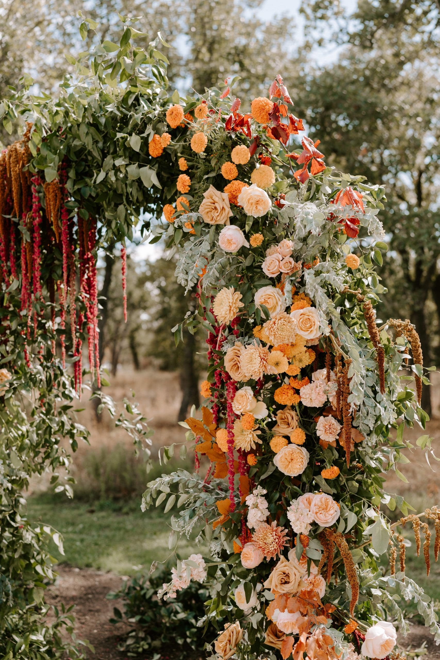 Boho floral arch featuring cream, orange, and burgundy flowers