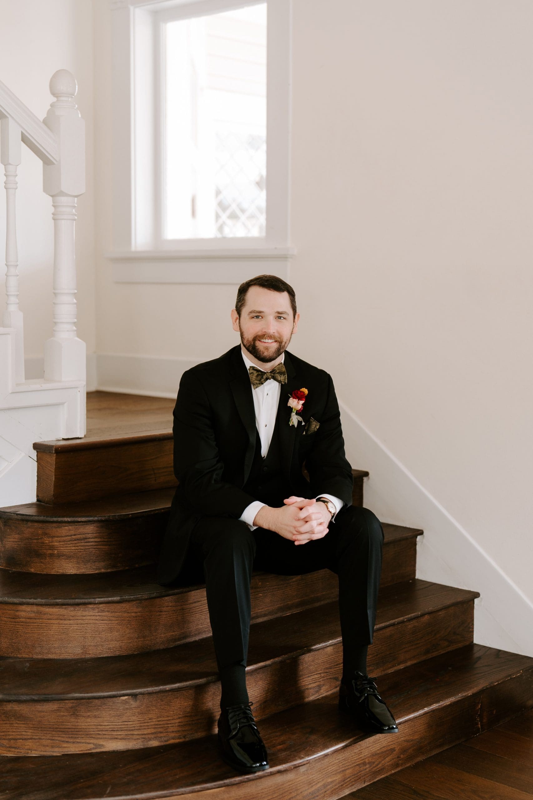 Groom wearing tux sitting on steps at The Grand Lady Austin