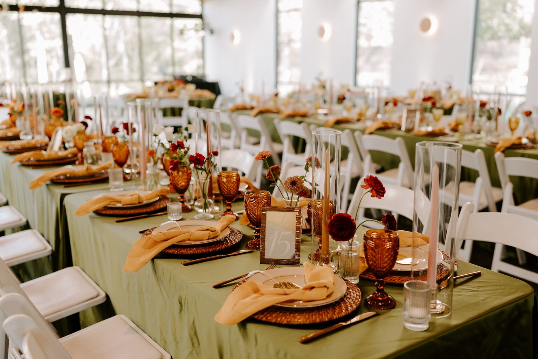 Boho wedding reception table with green table cloths, amber vintage glasses, and flowers in bud vases