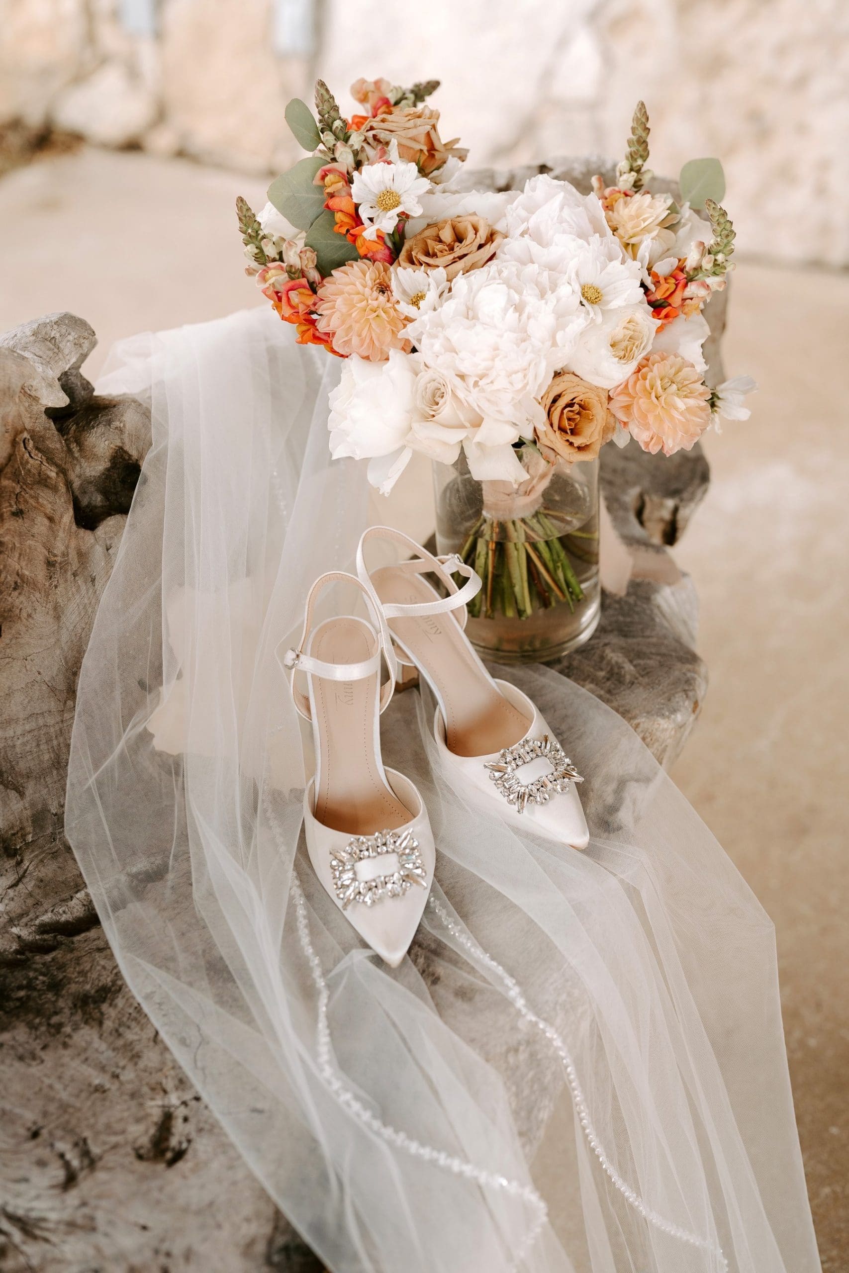 Boho bouquet sitting on bench next to veil with white wedding shoes on top of it