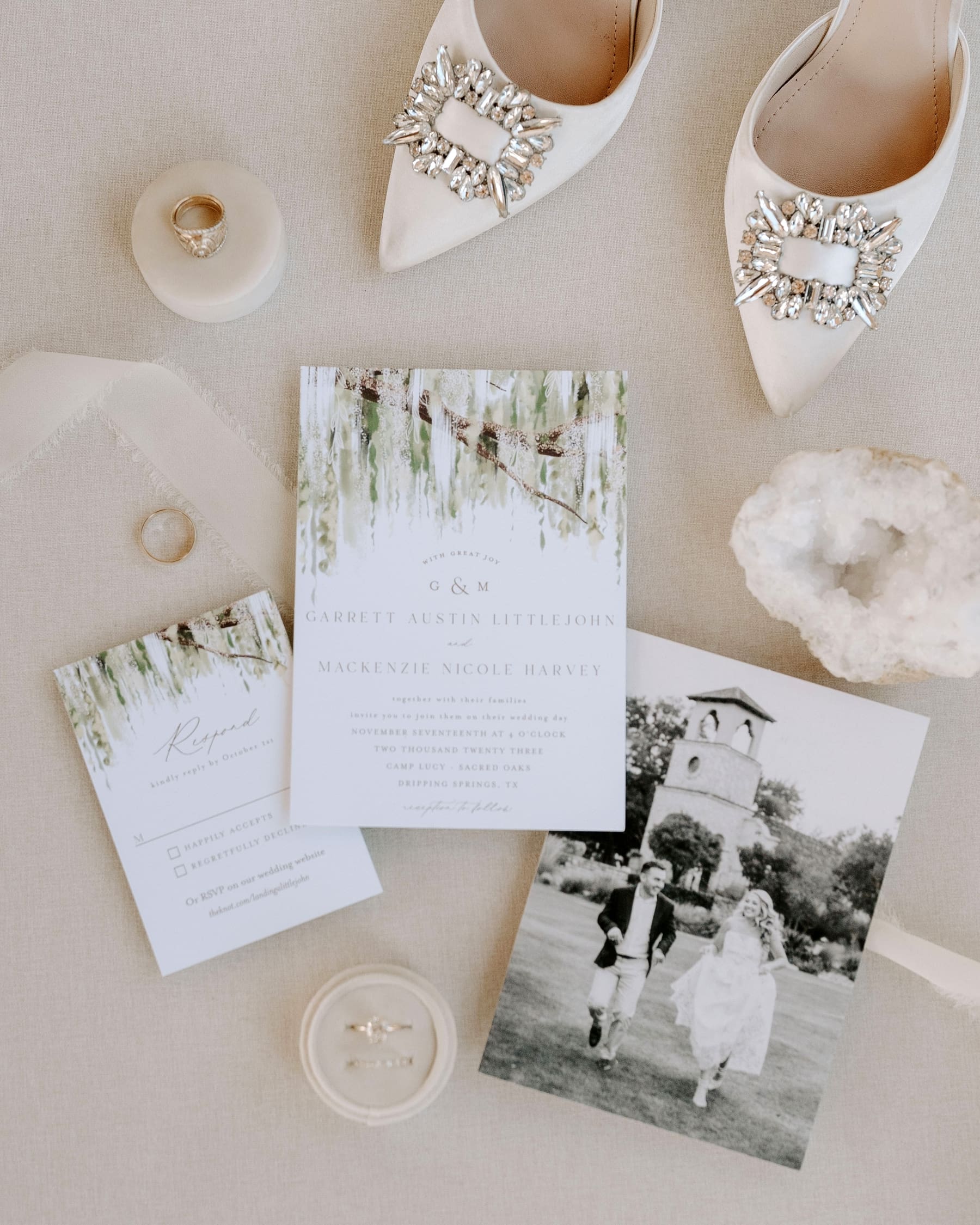 Flat lay featuring wedding invitation with weeping willow details, white wedding shoes with crystal details, and wedding rings