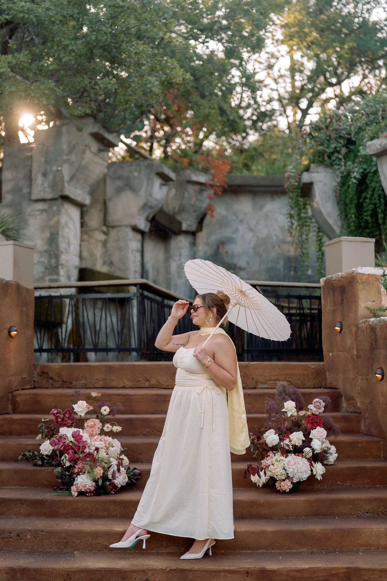 Bride posing on the Villa Antonia steps surrounded by colorful florals, holding a parasol during her anniversary photoshoot in the Texas Hill Country.