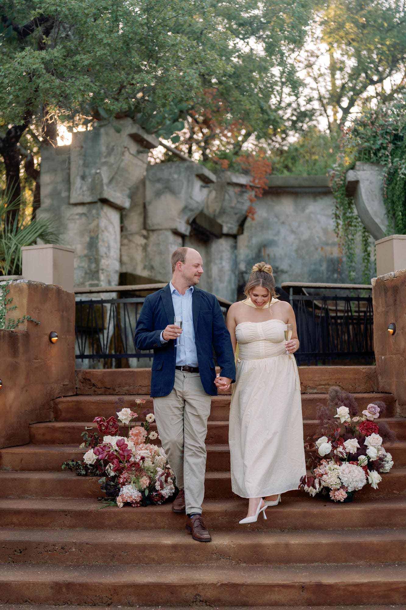 Couple walking hand in hand down the stone steps at Villa Antonia during their romantic anniversary session, with champagne glasses and floral arrangements nearby.