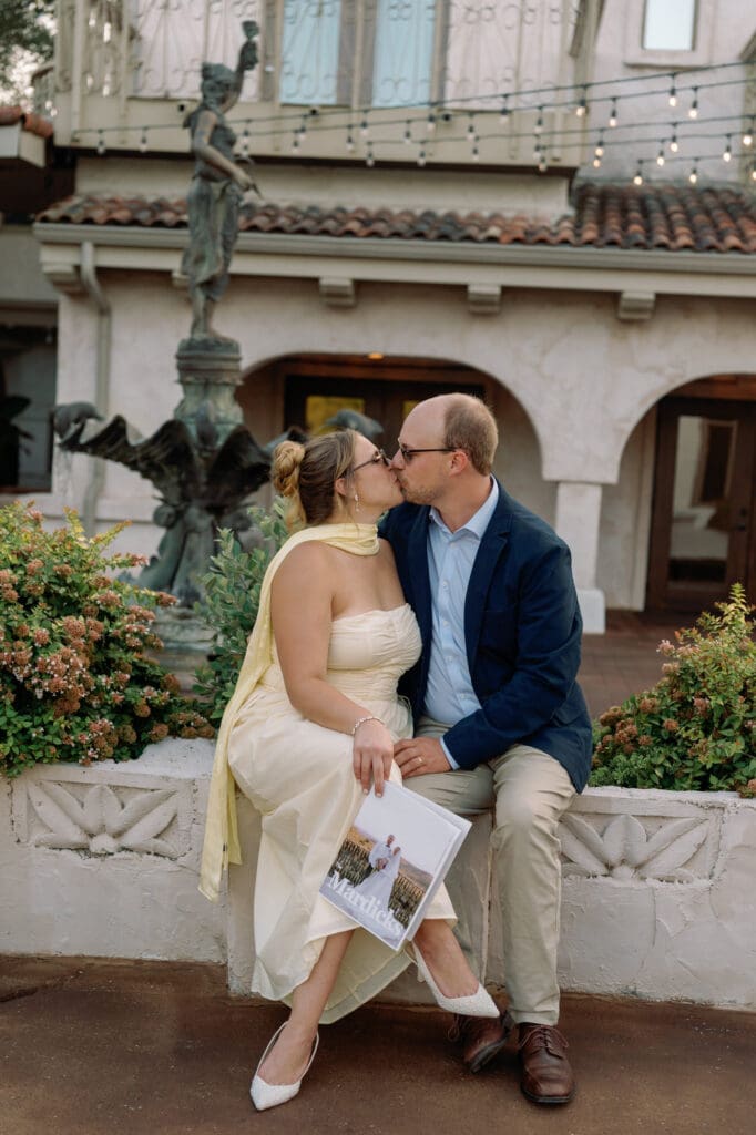 Couple sitting together, kissing with the bride holding custom magazines about their first year of marriage