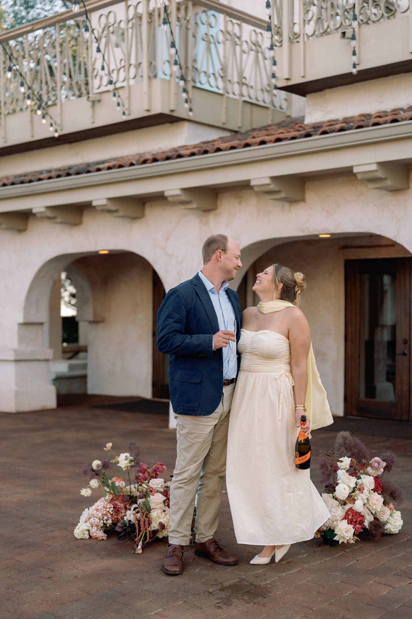 Couple celebrating their Villa Antonia anniversary session with champagne and florals, standing under string lights at the Tuscan-inspired Austin venue.